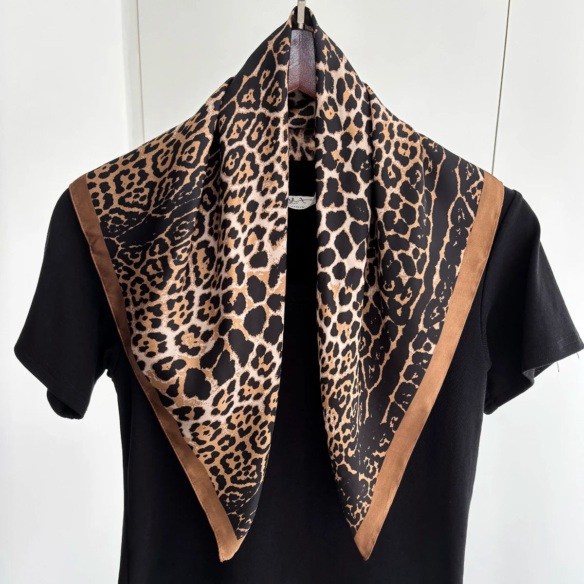 A black top styled with a leopard print silk scarf featuring brown trim.