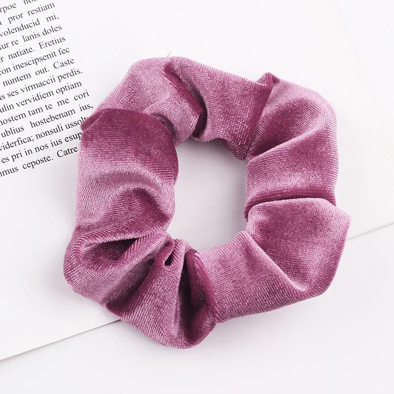 A close-up of a mauve velvet scrunchie with gathered fabric texture on a white background.