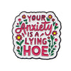 An enamel pin featuring text that reads Your Anxiety Is a Lying Hoe surrounded by floral elements.