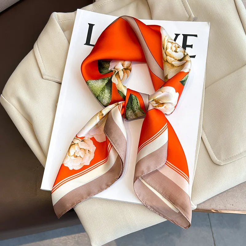 An orange and beige silk scarf tied in a bow, displayed on a white card against a light beige background.