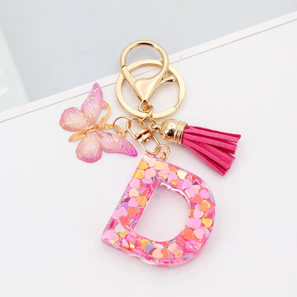 Gold acrylic letter keychain with a pink butterfly charm and a magenta tassel