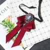 A deep red velvet bow tie with a silver rhinestone clasp and ribbon displayed on a checkered paper background.