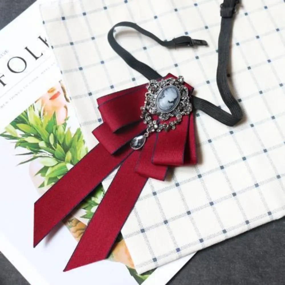 A deep red velvet bow tie with a silver rhinestone clasp and ribbon displayed on a checkered paper background.