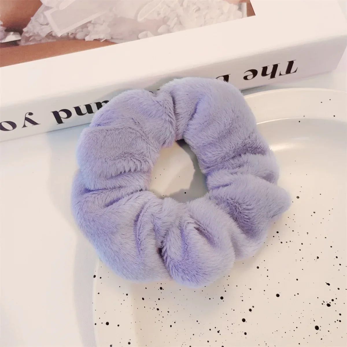 Un élastique pour cheveux en tricot flou lavande est exposé sur une surface blanche à côté d'un livre.