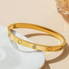 Goldplattiertes Edelstahlherzarmband-Set mit kleinen Diamantakzenten auf weißer Keramik.