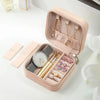 A pink leather jewelry travel organizer box open to reveal a watch, necklaces, and earrings.