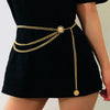 A gold diamond waist belt with chains is worn around the waist of a black dress.