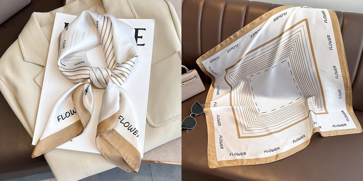 A beige silk scarf with a floral print and gold trim is displayed on a light-colored surface.