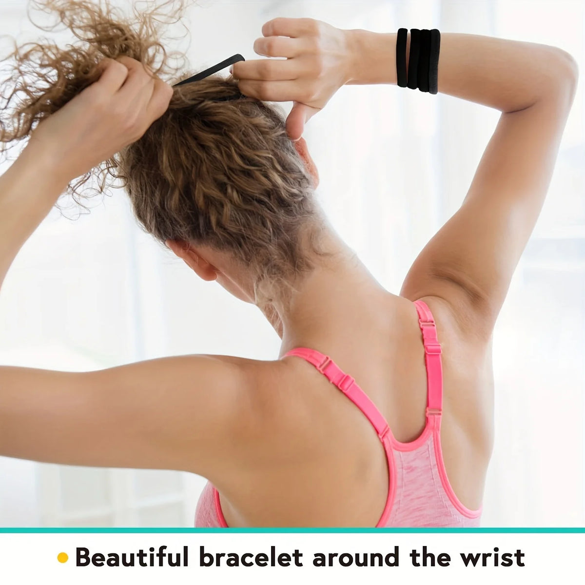 A person is tying a black elastic hair band around their hair while wearing a pink tank top.