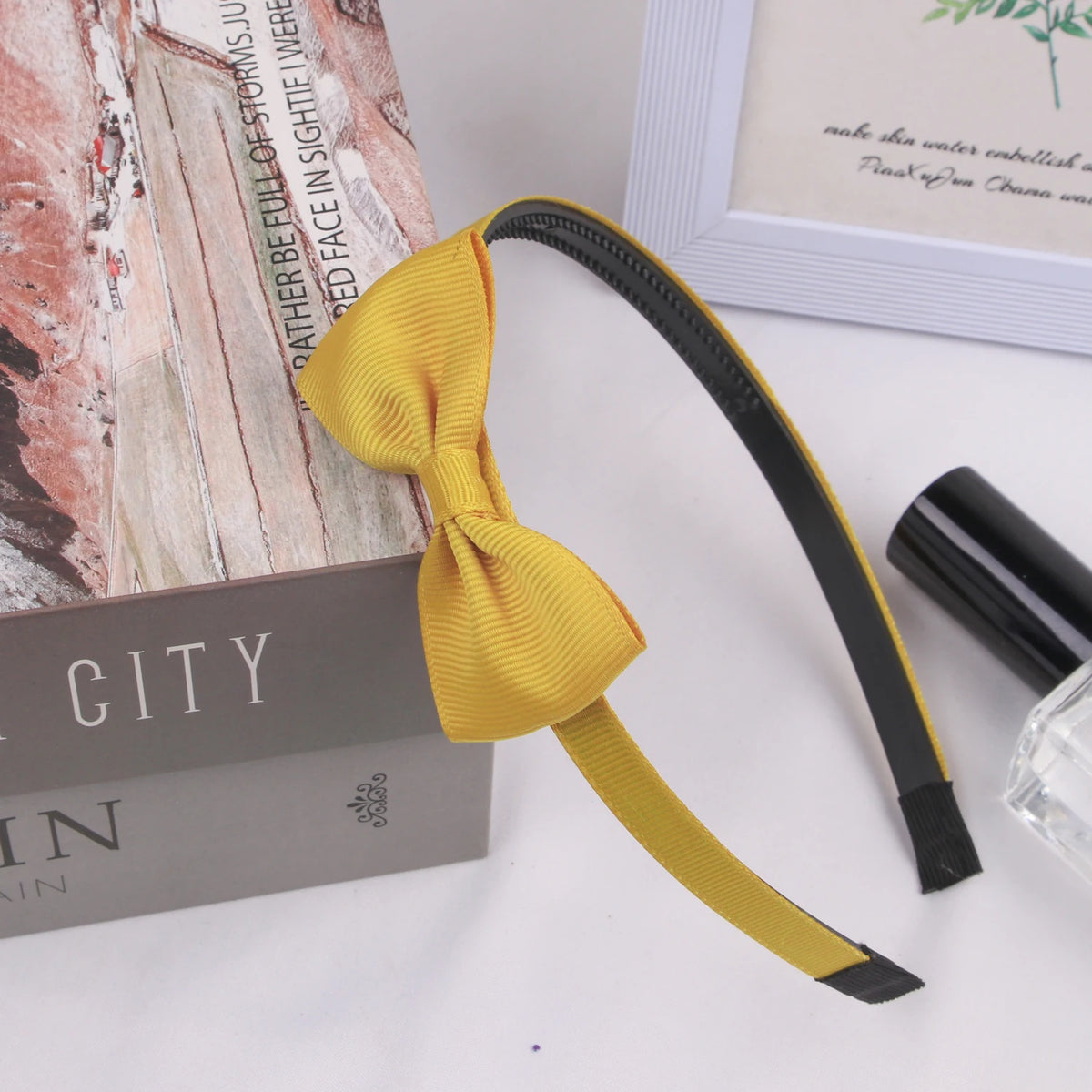 A yellow grosgrain ribbon hair bow is displayed next to a box and a framed card.