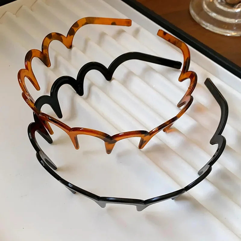 A headband made of brown resin with a wavy, toothed design, displayed on a white surface.
