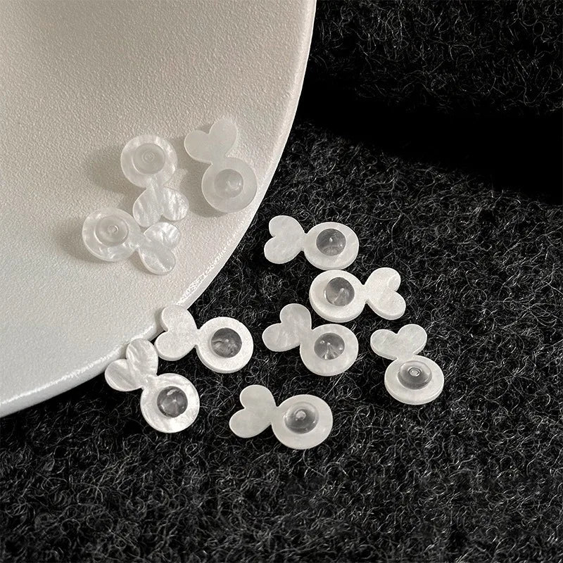 Clear silicone earring lifters shaped like hearts and circles resting on a white ceramic plate.