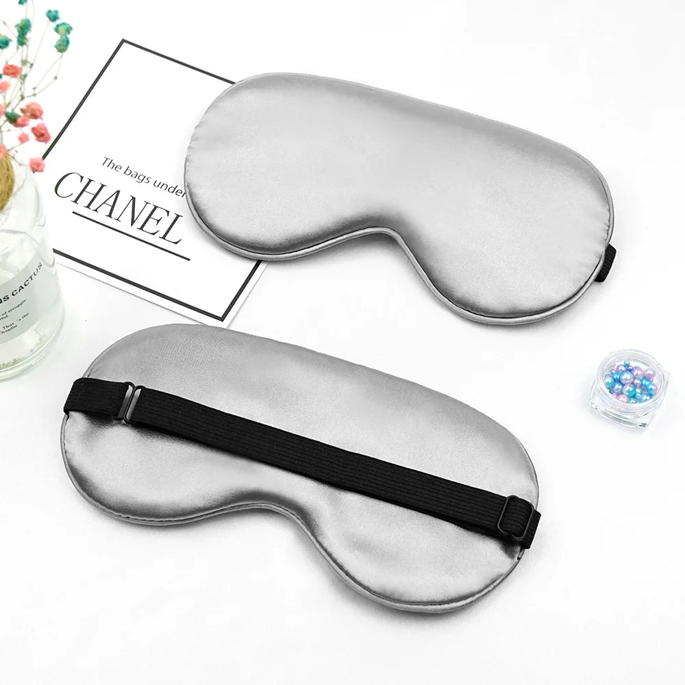 Silver silk sleep mask with a black strap shown next to a box labeled Chanel