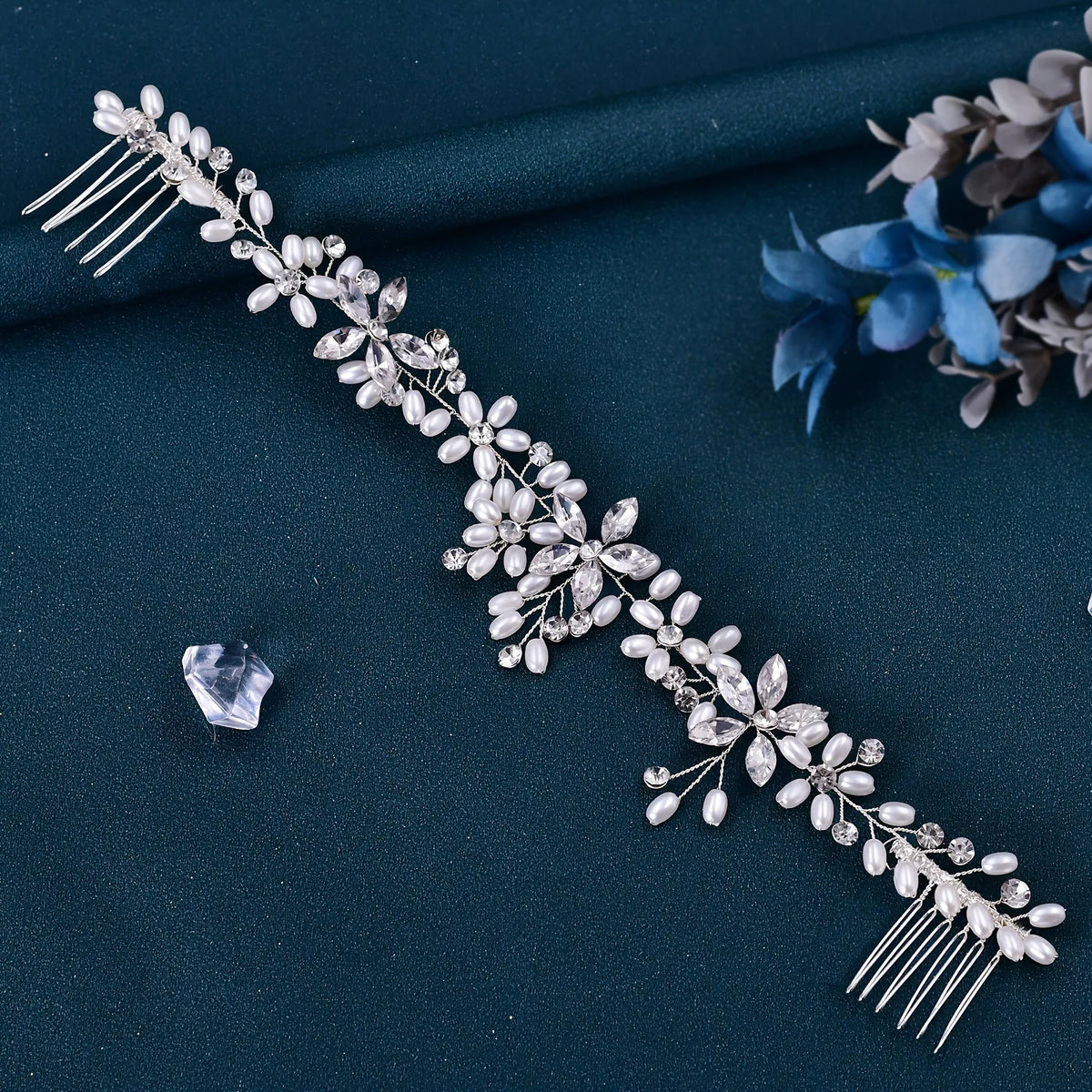 A delicate silver rhinestone bridal headband with floral and fringe details on a dark teal fabric.