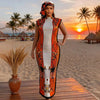 A plus size model wearing an orange and black African silk printed two-piece set on a sandy beach at sunset.