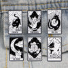 A set of six black and white enamel tarot cards featuring cats, a sun, the moon, and the wheel of fortune displayed on a deni