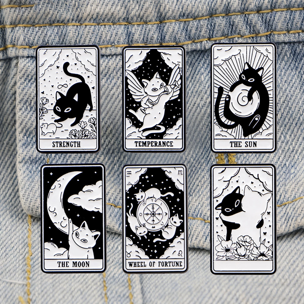 A set of six black and white enamel tarot cards featuring cats, a sun, the moon, and the wheel of fortune displayed on a deni