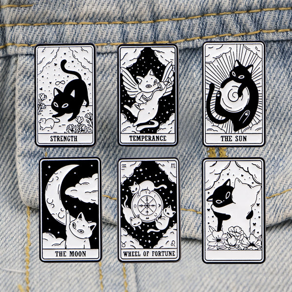 A set of six black and white enamel tarot cards featuring cats, a sun, the moon, and the wheel of fortune displayed on a deni