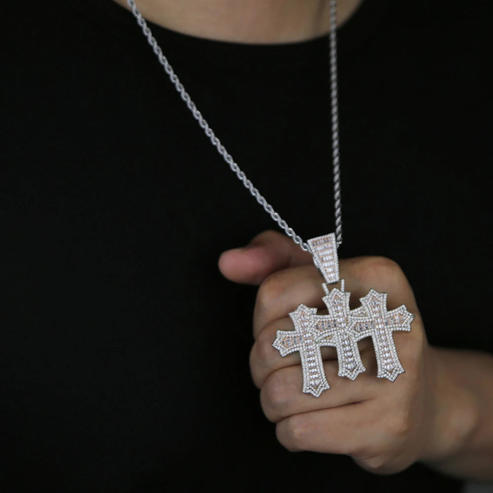 Une main tient un collier pendentif croix serti de glace sur fond noir.