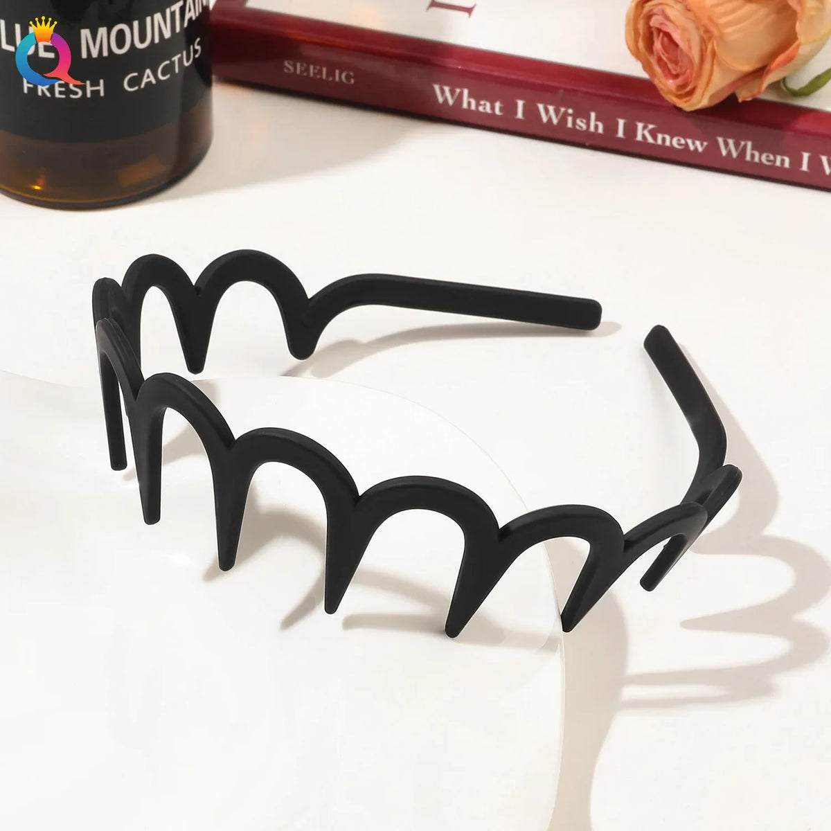 Black fashion acetate toothed headbands displayed on a white surface next to a book.