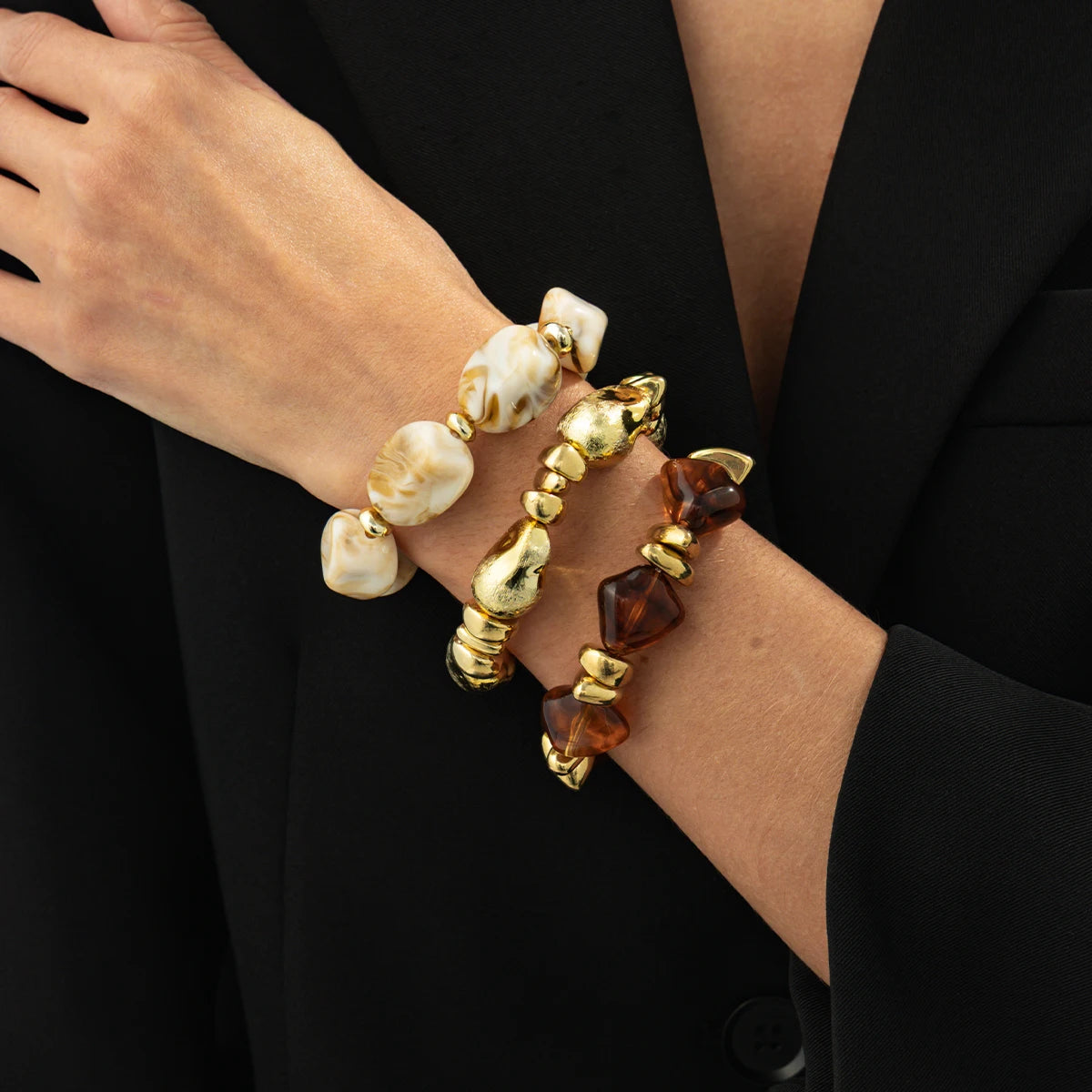 Une main portant un ensemble de bracelets de charme vintage en résine acrylique bohème avec des perles blanches et ambrées.