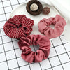 A display of three fabric scrunchies, including a red polka dot, a red and white checkered, and a satin pink one, alongside a