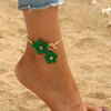 A gold-toned floral pendant necklace and earring set with green enamel flowers worn on a person's ankle.