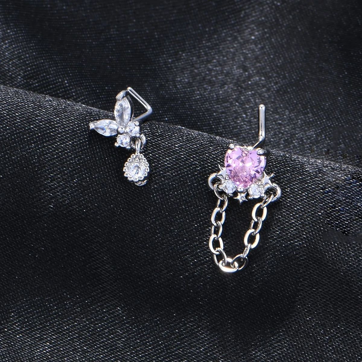 Une paire de anneaux à nez en acier inoxydable en forme de L avec un motif de fleur scintillante et un cœur de pierre rose.