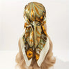 A rolled luxury satin silk scarf featuring an ornate gold and olive green paisley pattern tied around a blonde hairstyle.