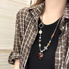A close-up of a woman wearing a brown plaid shirt and a beaded pendant necklace.