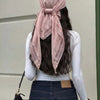 A woman with long dark hair wears a dusty rose shawl scarf with lace trim tied around her head and draped over a white long-s