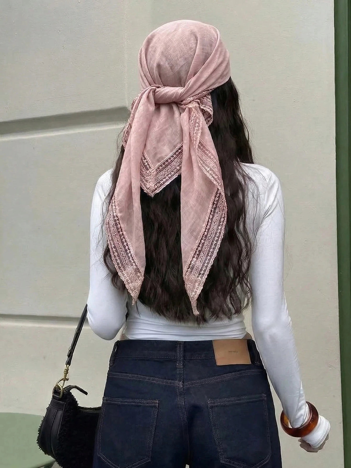 A woman with long dark hair wears a dusty rose shawl scarf with lace trim tied around her head and draped over a white long-s
