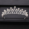A silver crystal bridal crown adorned with pearls and intricate branches, displayed on a dark surface.