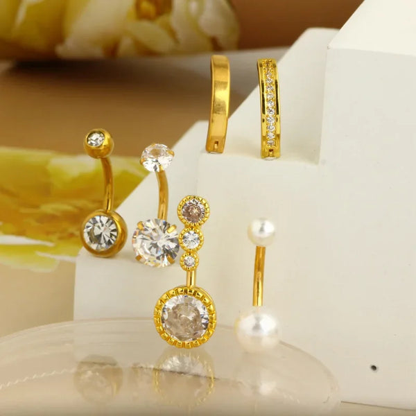 Gold-toned surgical stainless steel belly button rings and stud earrings displayed on a white surface.