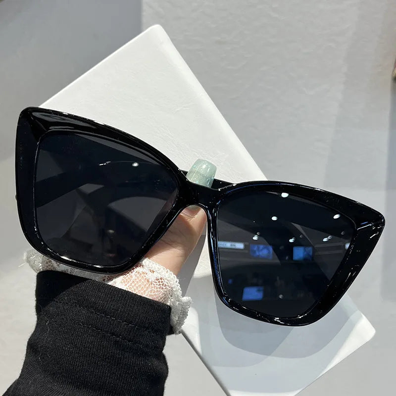 Black retro cat eye sunglasses with a light green detail resting on a white surface.