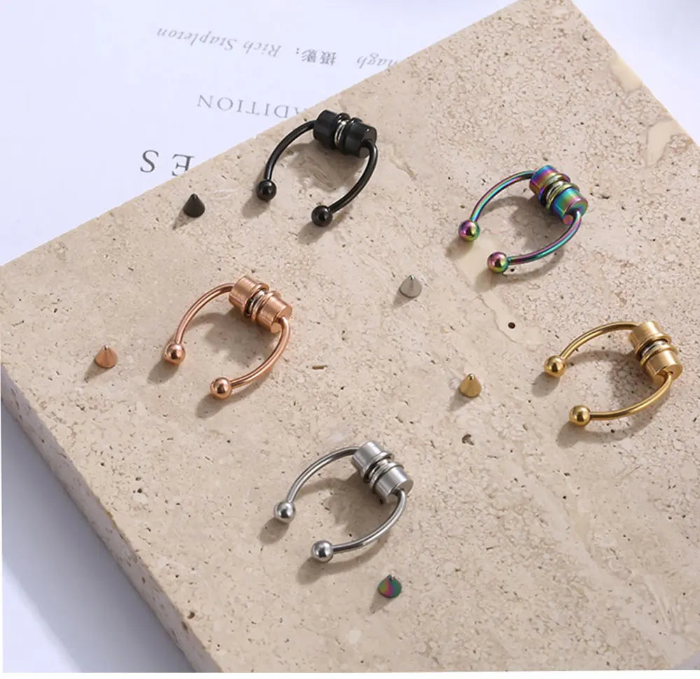 Sammlung von Edelstahl-Nasepiercing-Ringen in verschiedenen Größen und Finishes auf einem hellen Steinuntergrund