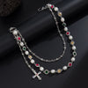 A silver necklace featuring pearl and gemstone beads, including a cross pendant, displayed on a dark background.