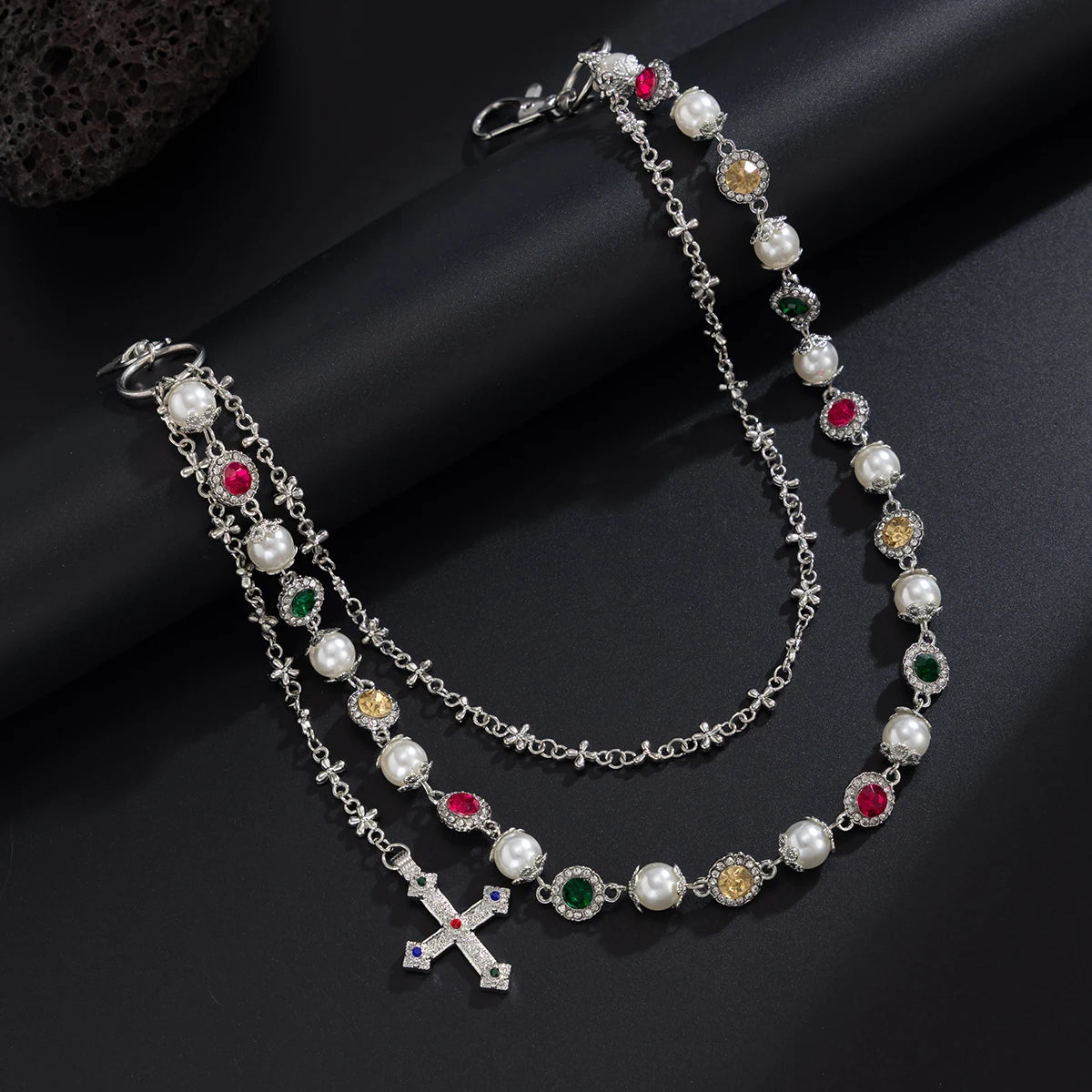 A silver necklace featuring pearl and gemstone beads, including a cross pendant, displayed on a dark background.