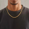A close-up of a gold rope charm necklace worn around the neck against a dark shirt.