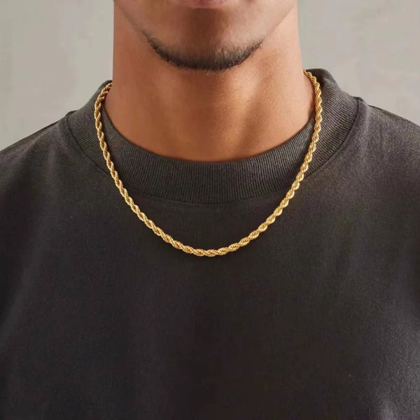 A close-up of a gold rope charm necklace worn around the neck against a dark shirt.