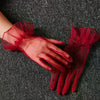 A hand wearing sheer red lace tulle finger gloves resting on a dark gray fabric.