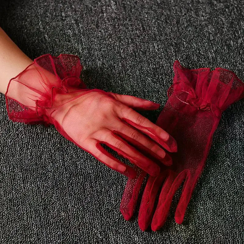 A hand wearing sheer red lace tulle finger gloves resting on a dark gray fabric.