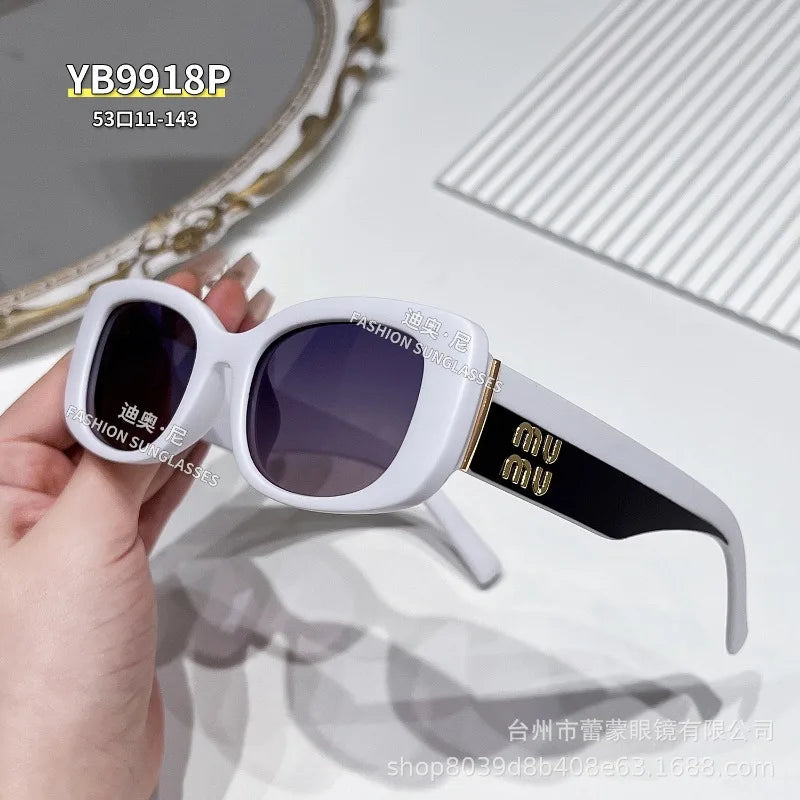 A pair of white sunglasses with dark lenses and gold accents are held in a hand against a light background.