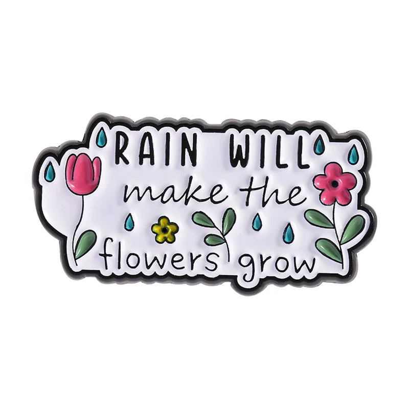 An enamel pin featuring the quote Rain will make the flowers grow with illustrations of tulips and flowers.
