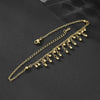 Collar de tobillo dorado hecho de cuentas redondas y una cadena, mostrado contra un fondo oscuro.