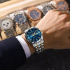 A close-up of a luxury men's blue quartz watch with a luminous dial resting on a wooden display with other watches.