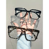 Una mano sostiene unas gafas cuadradas transparentes con montura negra y un par de gafas de estampado de leopardo.