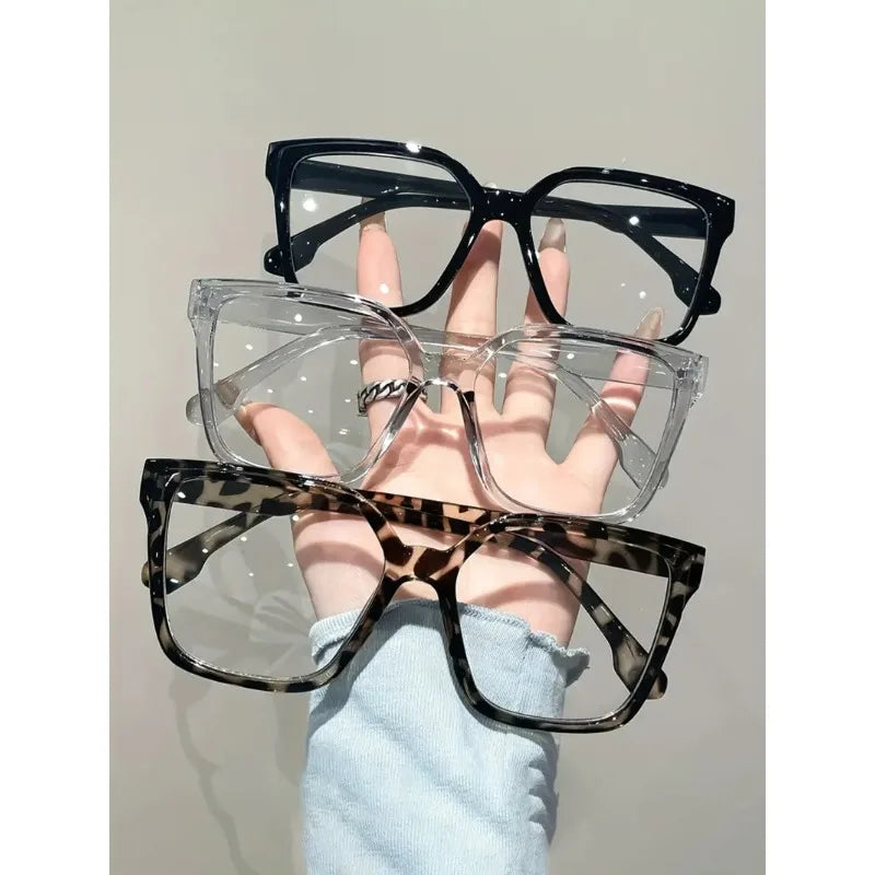 Una mano sostiene unas gafas cuadradas transparentes con montura negra y un par de gafas de estampado de leopardo.