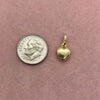 A gold plated butterfly key pendant charm resting on a pink background next to a silver coin.