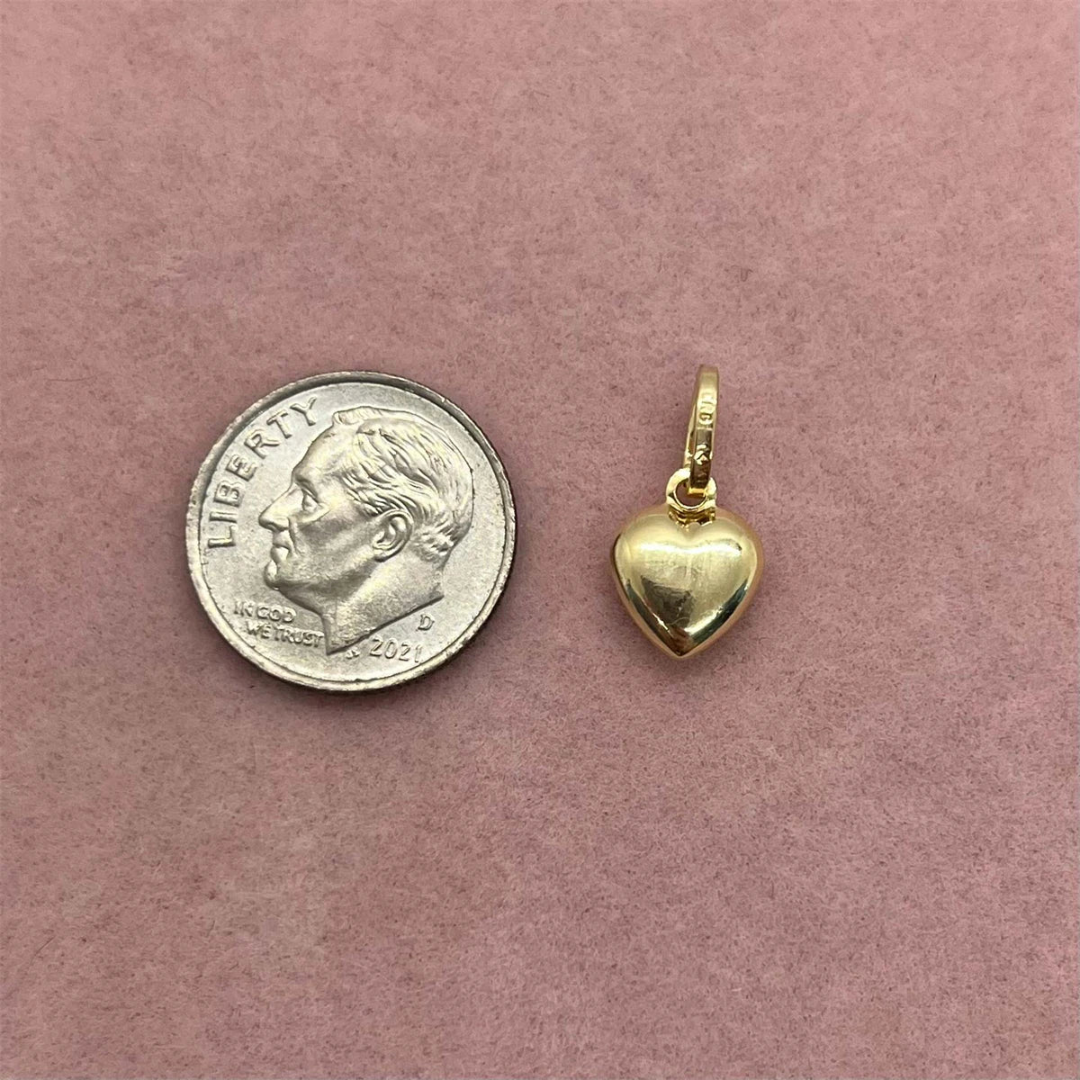 A gold plated butterfly key pendant charm resting on a pink background next to a silver coin.
